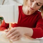 A dedicated female seamstress works on a sewing machine creating a red dress indoors.
