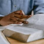 A person wearing a blue shirt flipping through a Bible, highlighting faith and study.