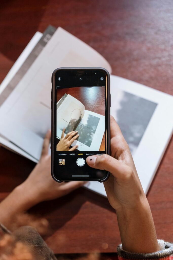 Person photographing a book with a smartphone indoors on a wooden table.
